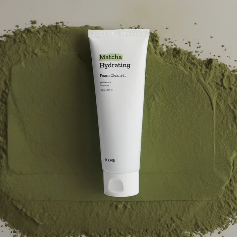 Tubo blanco de B:Lab Matcha Hydrating Foam Cleanser sobre polvo de matcha